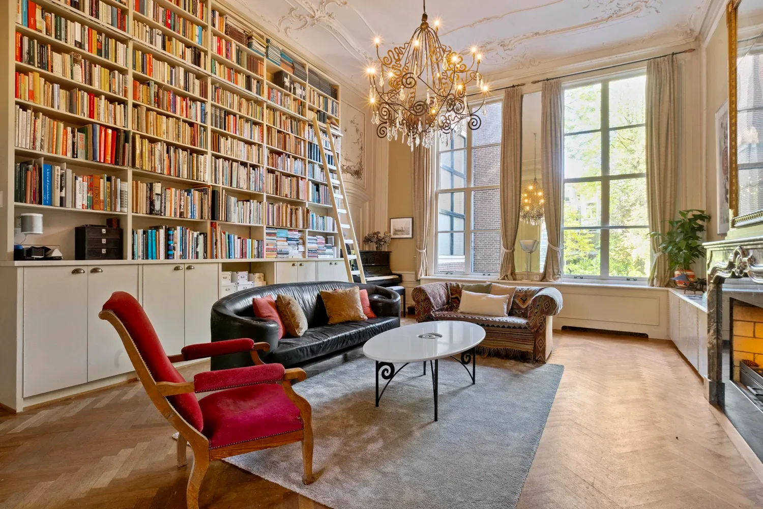 Weelderige woonkamer met boekenwand, kroonluchter en hoge ramen — Keizersgracht Amsterdam